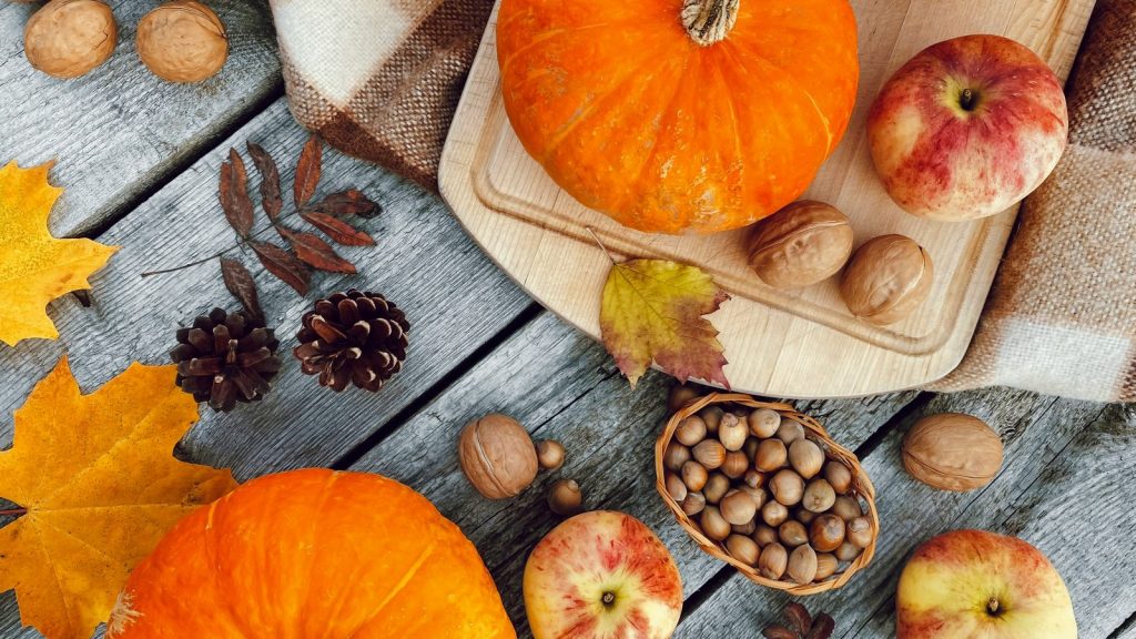 Herbstliches Flatlay mit Kürbissen, Äpfeln, Walnüssen und Haselnüssen auf Holzbrett