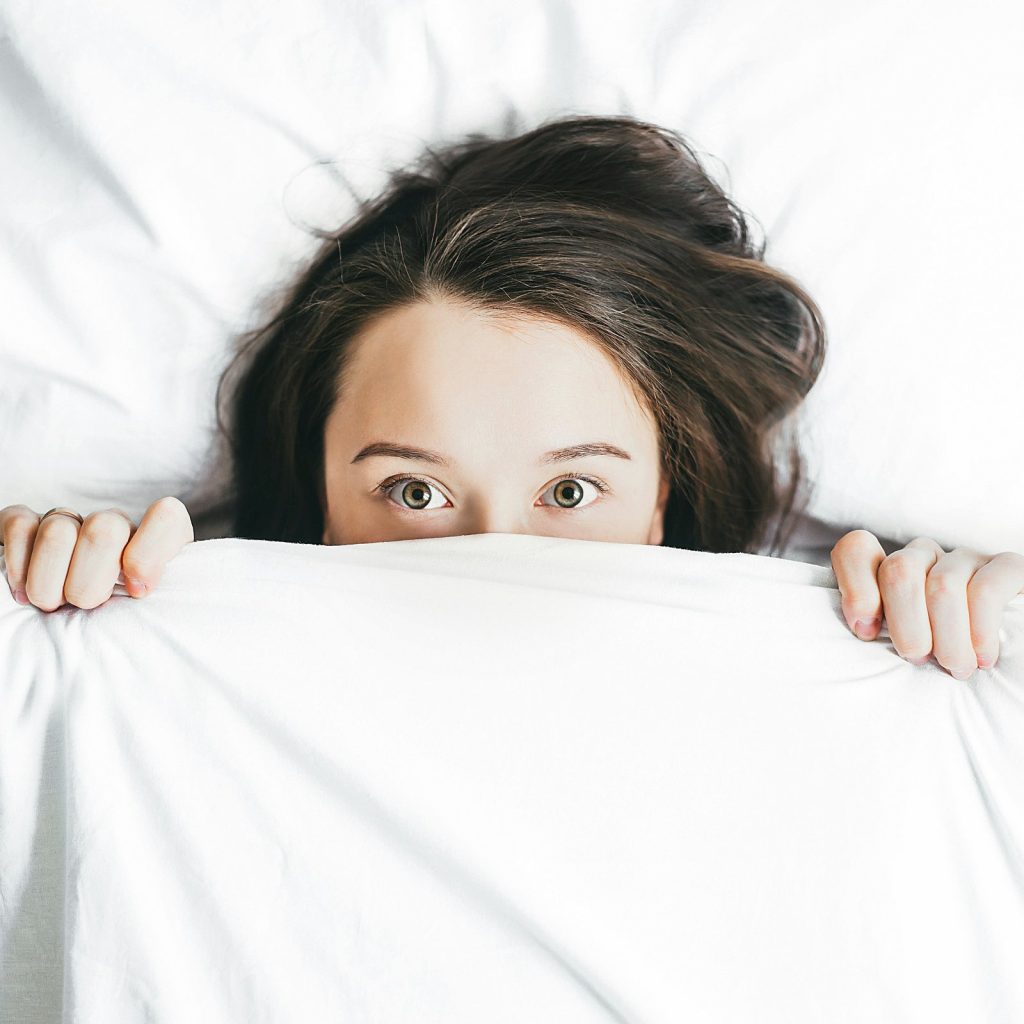 Frau liegt wach im Bett und schaut mit weit geöffneten Augen über die Bettdecke