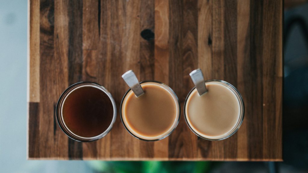 Drei Gläser Kaffee von oben auf einem Holztisch: schwarz, mit wenig und mit mehr Milch