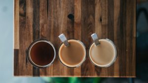 Drei Gläser Kaffee von oben auf einem Holztisch: schwarz, mit wenig und mit mehr Milch