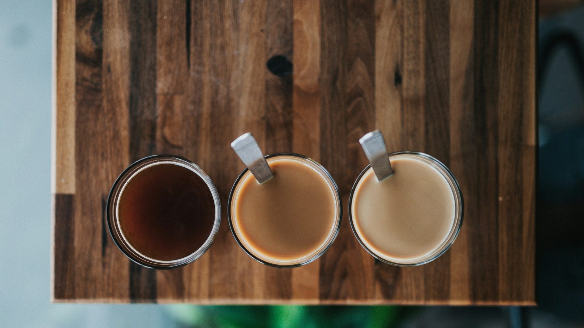 Drei Gläser Kaffee von oben auf einem Holztisch: schwarz, mit wenig und mit mehr Milch