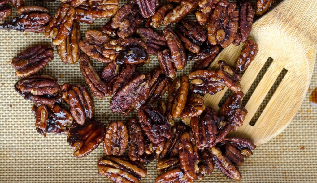 Karamellisierte Pekannüsse auf einem Backblech mit Silikonmatte und Holzspatel